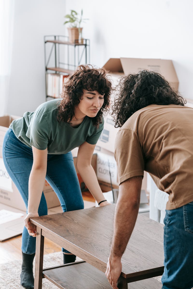 Couple lifting a wooden table while moving into a new home illuminated by daylight.